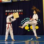 10. Uczennica ubrana w strój taekwondo wykonuje kopnięcie z wyskoku celując w deskę trzymaną przed drugą uczennicę..jpg