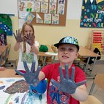 uczniowie podczas zajęć sensoplastyki prezentują pomalowane farbą dłonie.jpg