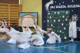 taniec dzieci przebranych w białe stroje ze skrzydłami, na tle dekoracji przedstawiajacej stajenkę i gwiazdy.JPG