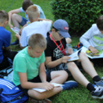 Uczniowie klasy 4 SP czytają książki siedząc na trawie.png